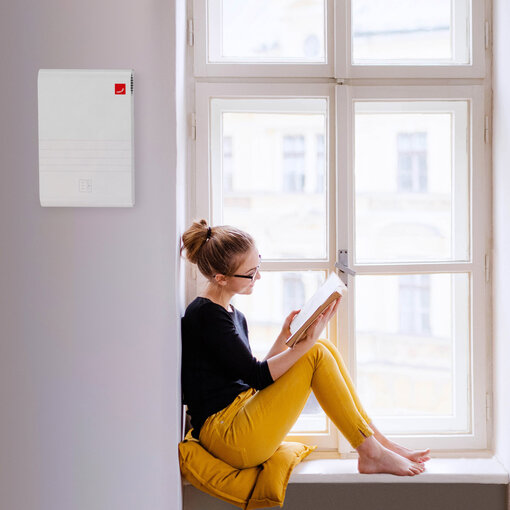 A young happy college female student with a book sitting on window sill at home, studying.