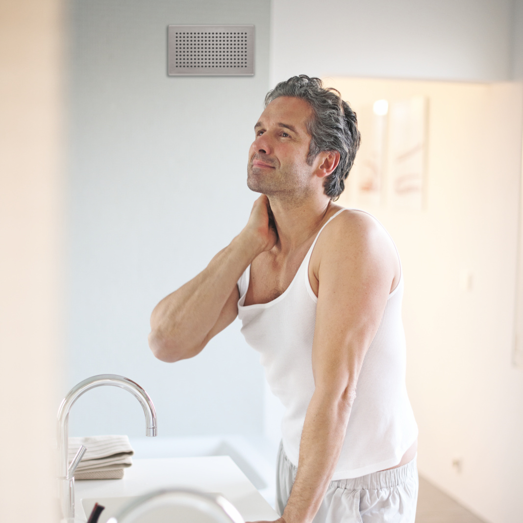 Griglia di design Zehnder Diffusore dell'aria di scarico in bagno. Uomo davanti allo specchio