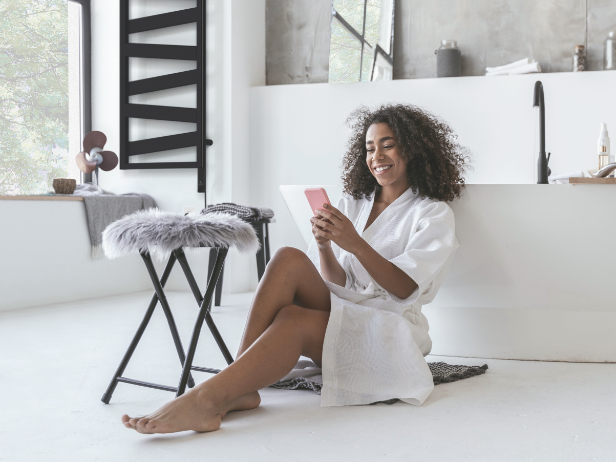Smiling woman sitting in the bathroom on the floor with a smartphone in her hands