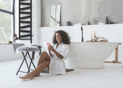 Zehnder_RAD_Ribbon-EL_zeh-nih-keyvisual-300dpi-cmyk Smiling woman sitting in the bathroom on the floor with a smartphone in her hands